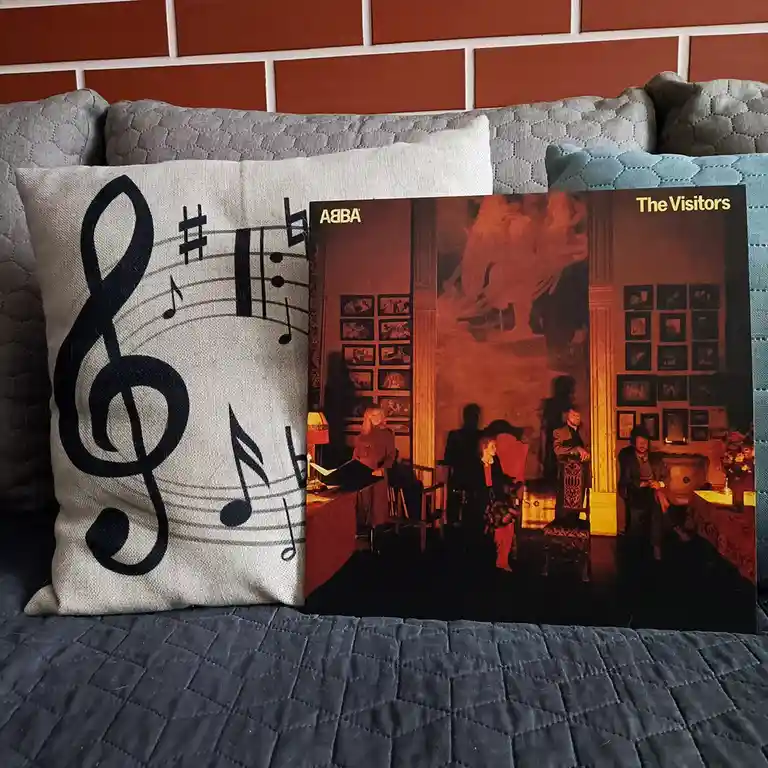 A photo shows a beige pillow with a large black treble clef and musical notes next to a physical copy of ABBA's 'The…
