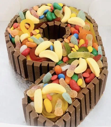 A large, three-dimensional number '9' cake made from Kit Kat bars forming the outline and filled with colorful gummy candies…