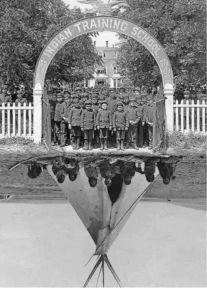 A historical black-and-white photo shows a group of children in uniform standing under an archway labeled 'INDIAN TRAINING…