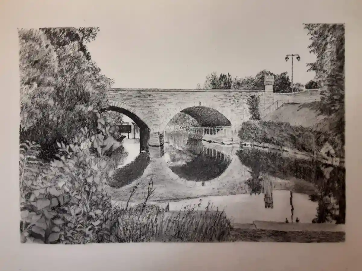 A black-and-white pencil sketch depicts a stone bridge with two arches spanning a calm canal, surrounded by dense foliage…