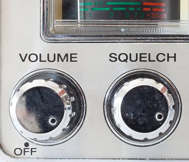A close-up of a vintage radio's control panel showing two knobs labeled 'VOLUME' and 'SQUELCH', with the 'VOLUME' knob…