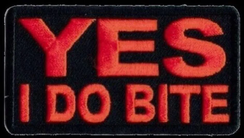 A black rectangular patch with bold red embroidered text that reads 'YES' on the top line and 'I DO BITE' on the bottom…