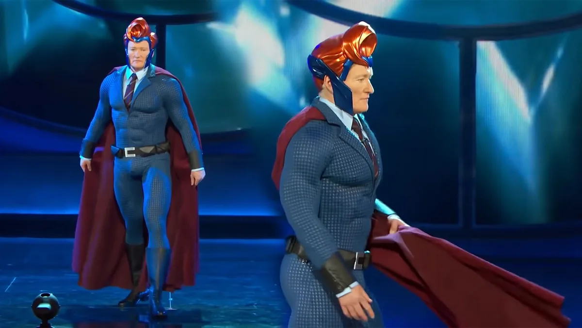 Two identical figures of Conan O'Brien in a blue superhero costume with a red cape and a large orange helmet walk side by…