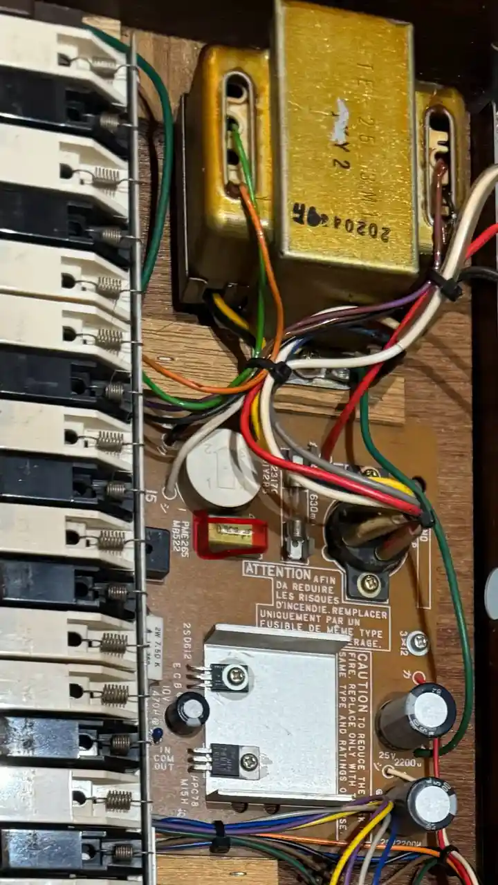 A close-up photo of a cluttered, messy electrical panel with numerous colorful wires, circuit breakers, and components. A…