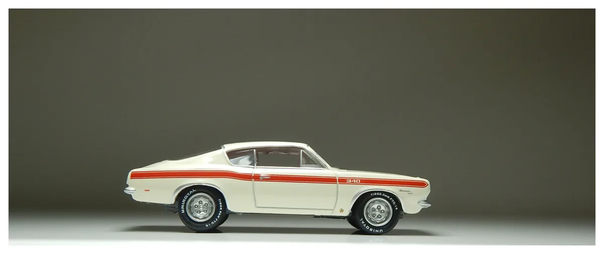 A white die-cast model of a classic American muscle car, likely a Plymouth Road Runner, is shown in profile against a plain…