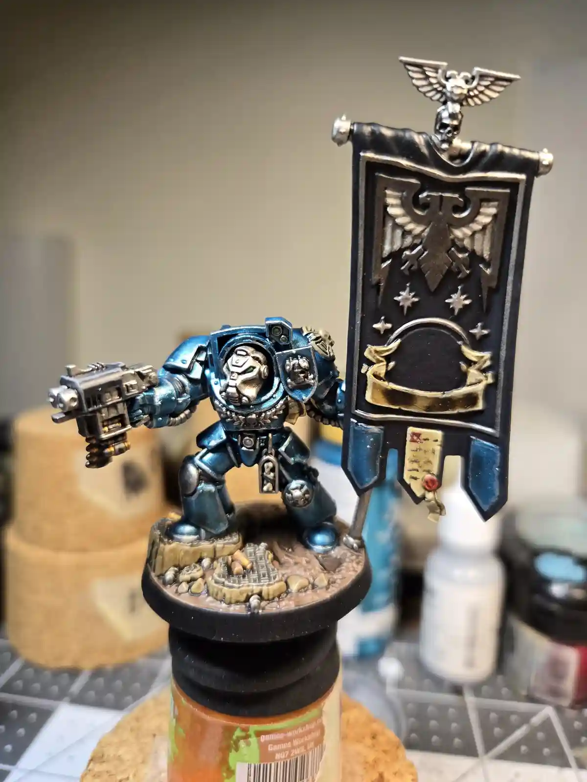 A highly detailed, hand-painted Warhammer 40,000 Space Marine miniature in blue armor, holding a weapon and a banner, is…
