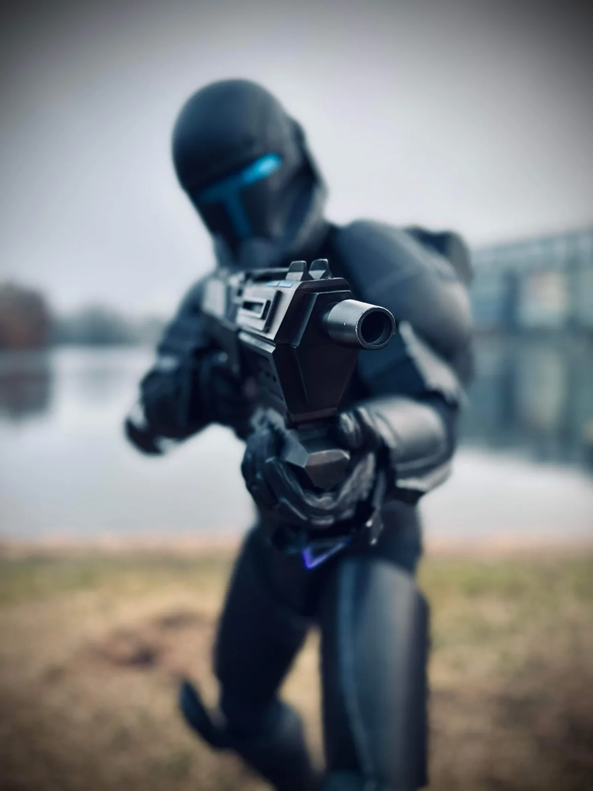 A person in a black futuristic combat suit with glowing blue visor and armor is aiming a large sci-fi weapon directly at the…