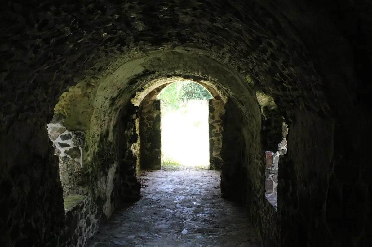 A dim, stone-walled tunnel with an arched ceiling leads to a bright, sunlit exit. The image is overlaid with the text 'i'm…