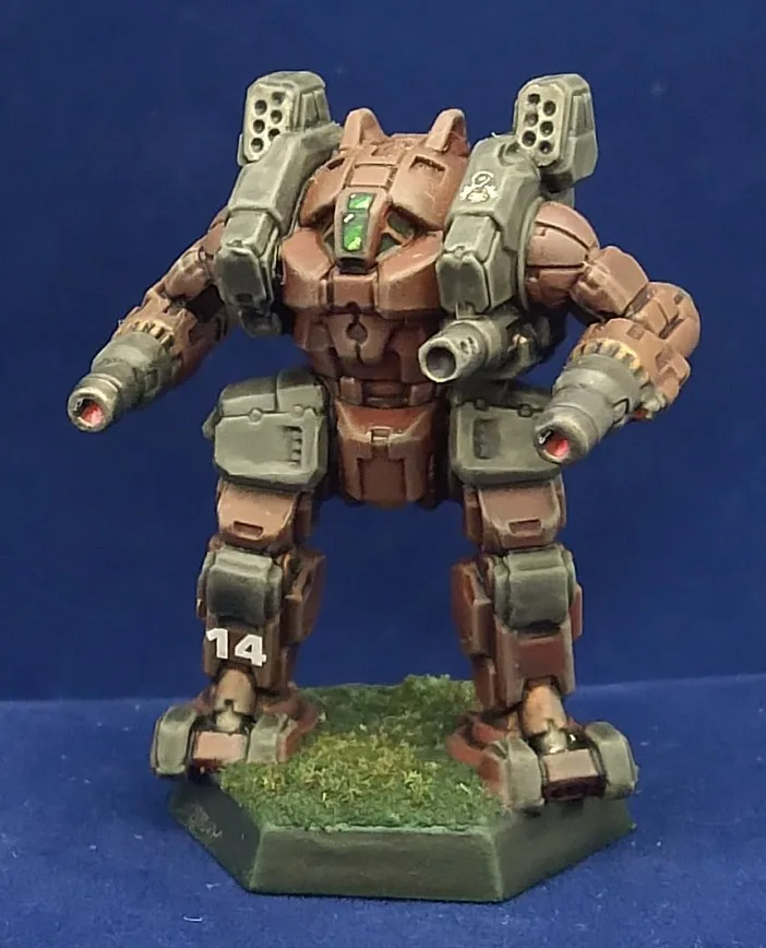 A painted miniature of a heavily armed, bipedal mech with brown and grey armor, glowing green eyes, and red-tipped cannons…