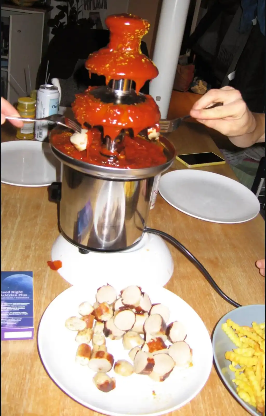 A stainless steel fondue pot is repurposed as a multi-tiered fountain overflowing with red tomato sauce and sprinkled with…