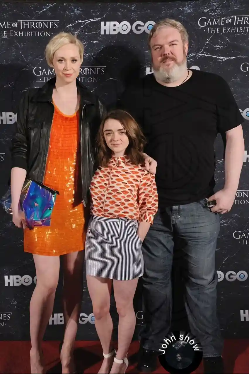 Three people pose together at a 'Game of Thrones: The Exhibition' event, with a circular watermark in the bottom right…