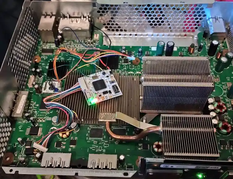 A close-up photo of an open computer motherboard with visible circuitry, capacitors, heat sinks, and copper pipes. A small…