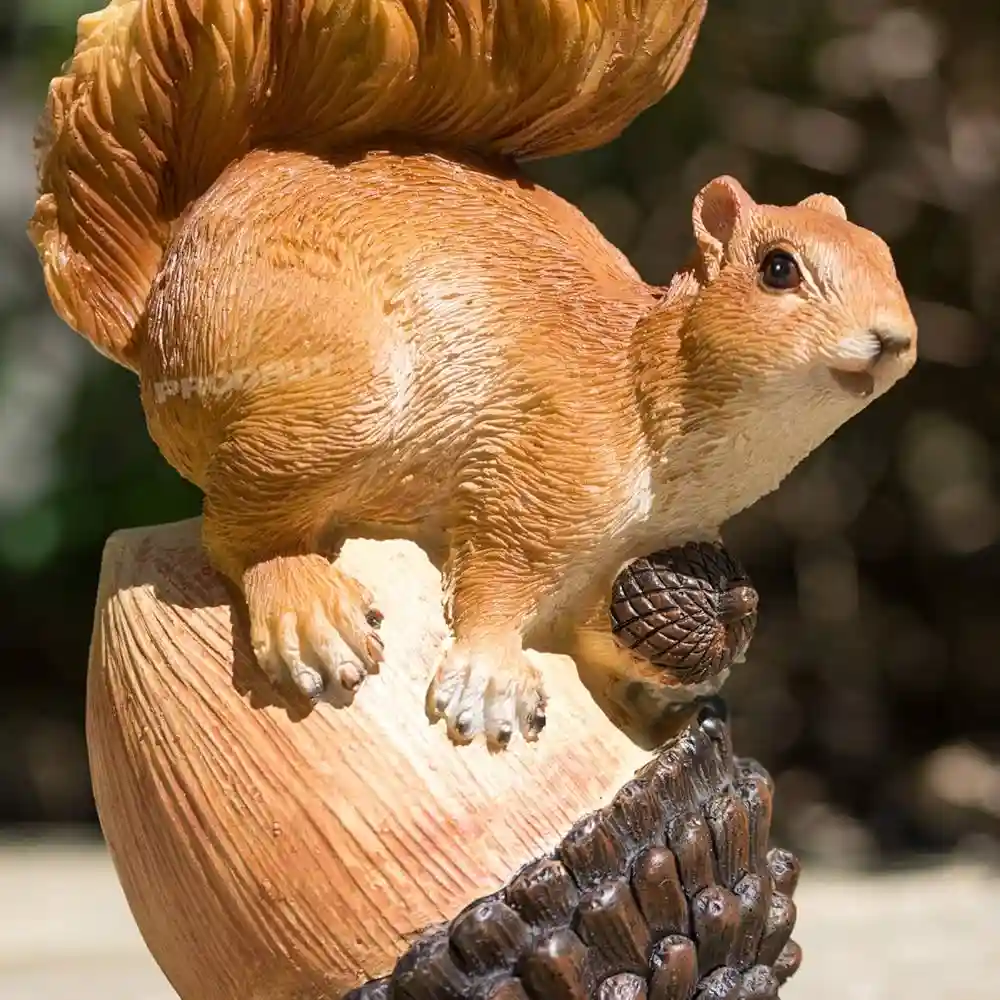 A close-up of a detailed plastic statue of a brown squirrel perched atop a large pinecone, holding a smaller pinecone in its…