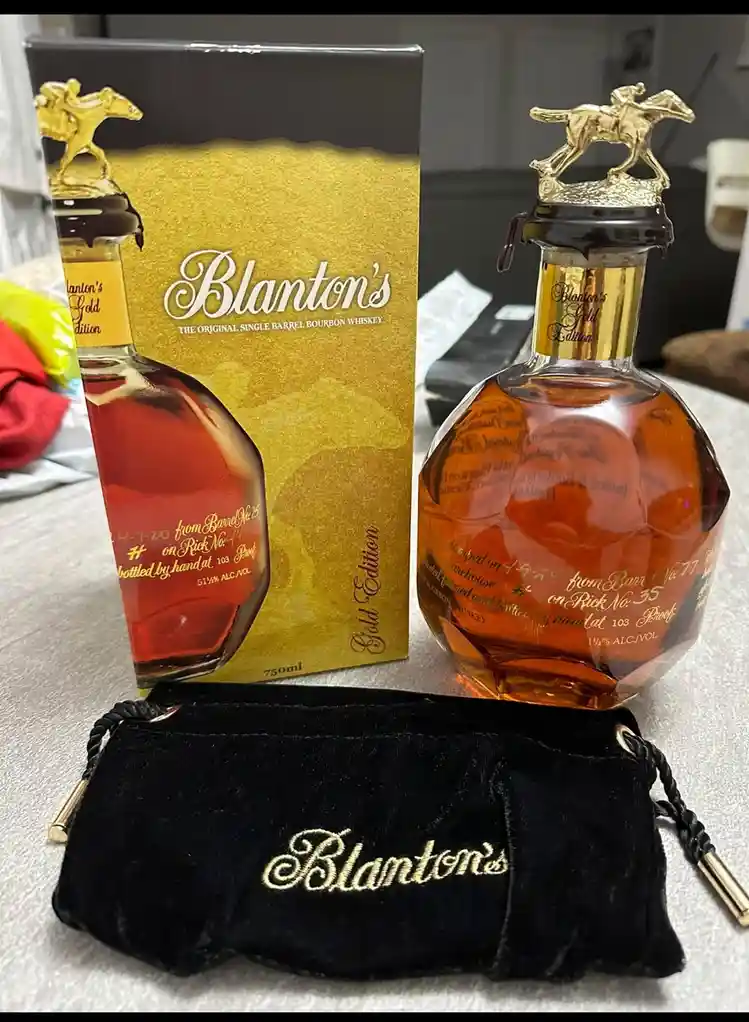 A bottle of Blanton's Gold Edition bourbon whiskey sits next to its gold and black box and a black velvet pouch with the…