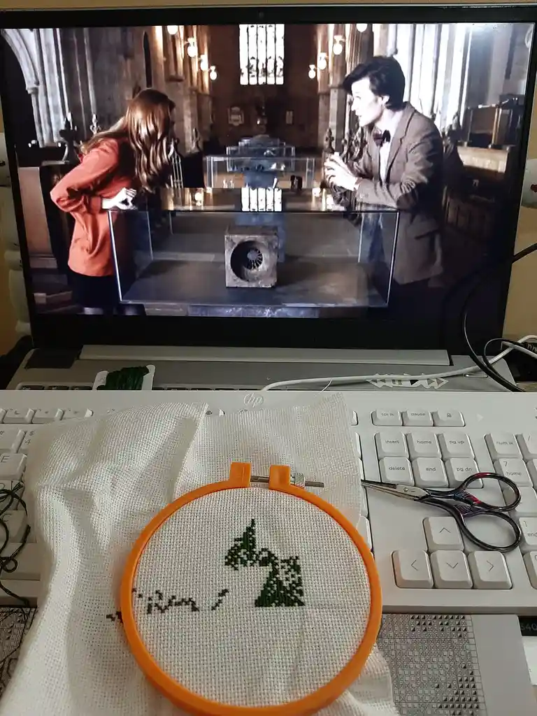 A laptop screen displays a scene from Doctor Who featuring the Doctor and Clara in a museum-like setting, with a mysterious…