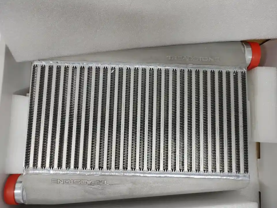 A silver intercooler with 'TREADSTONE' embossed on both ends sits nestled in white foam packaging, featuring a grid of…