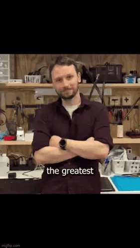 A man in a maroon shirt stands with arms crossed in a workshop, then the image zooms in on his face, then his nose, with…
