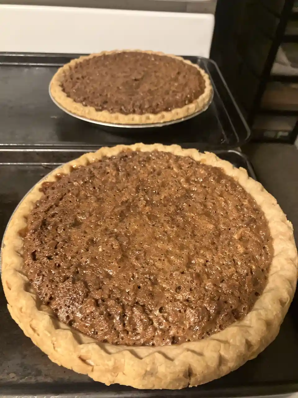 Two freshly baked pecan pies sit on baking sheets, one noticeably larger than the other, with the text overlay stating 'i…