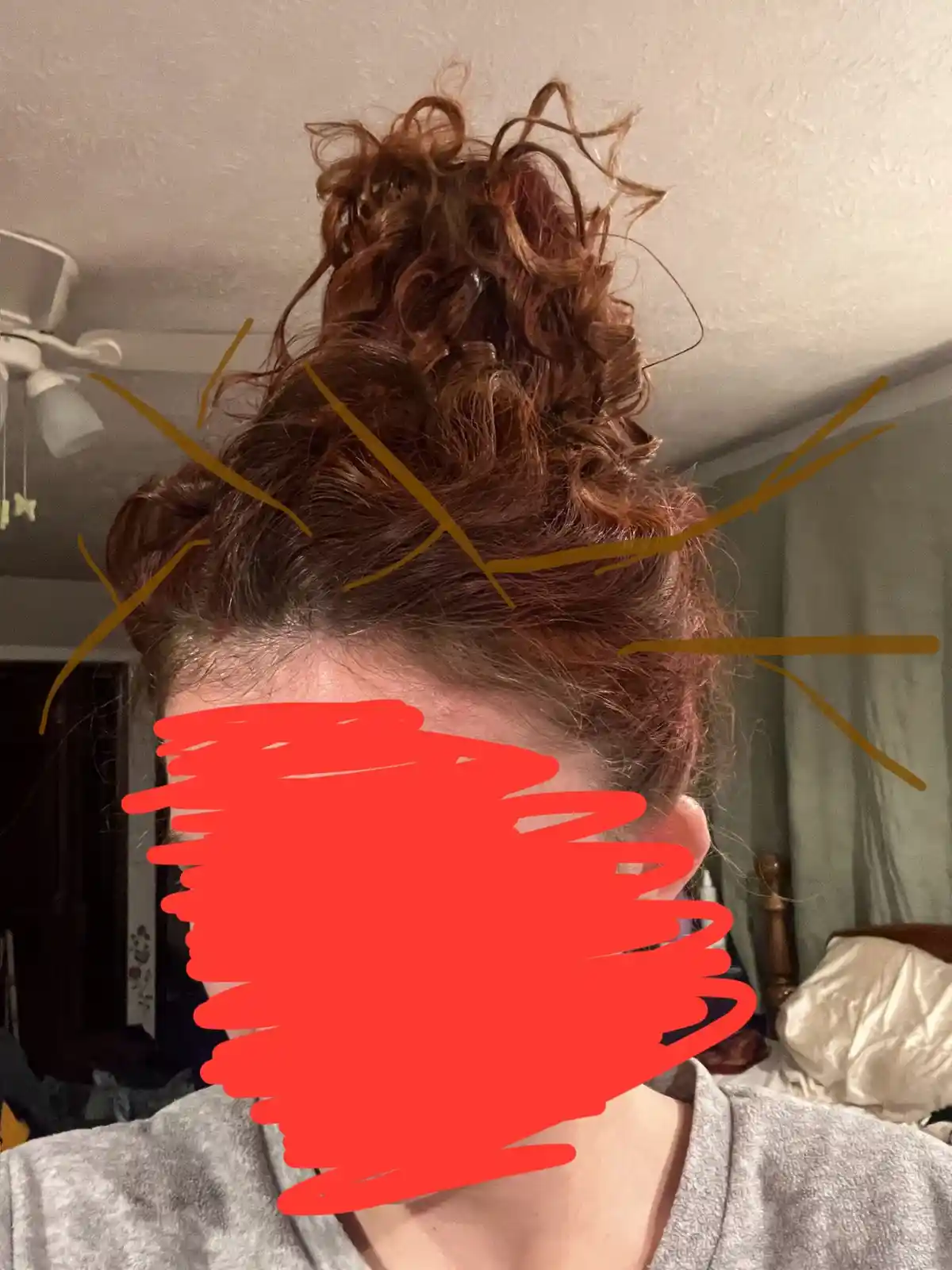 A person's messy, curly brown hair is styled in a high, disheveled bun, with the face obscured by a red scribble and yellow…