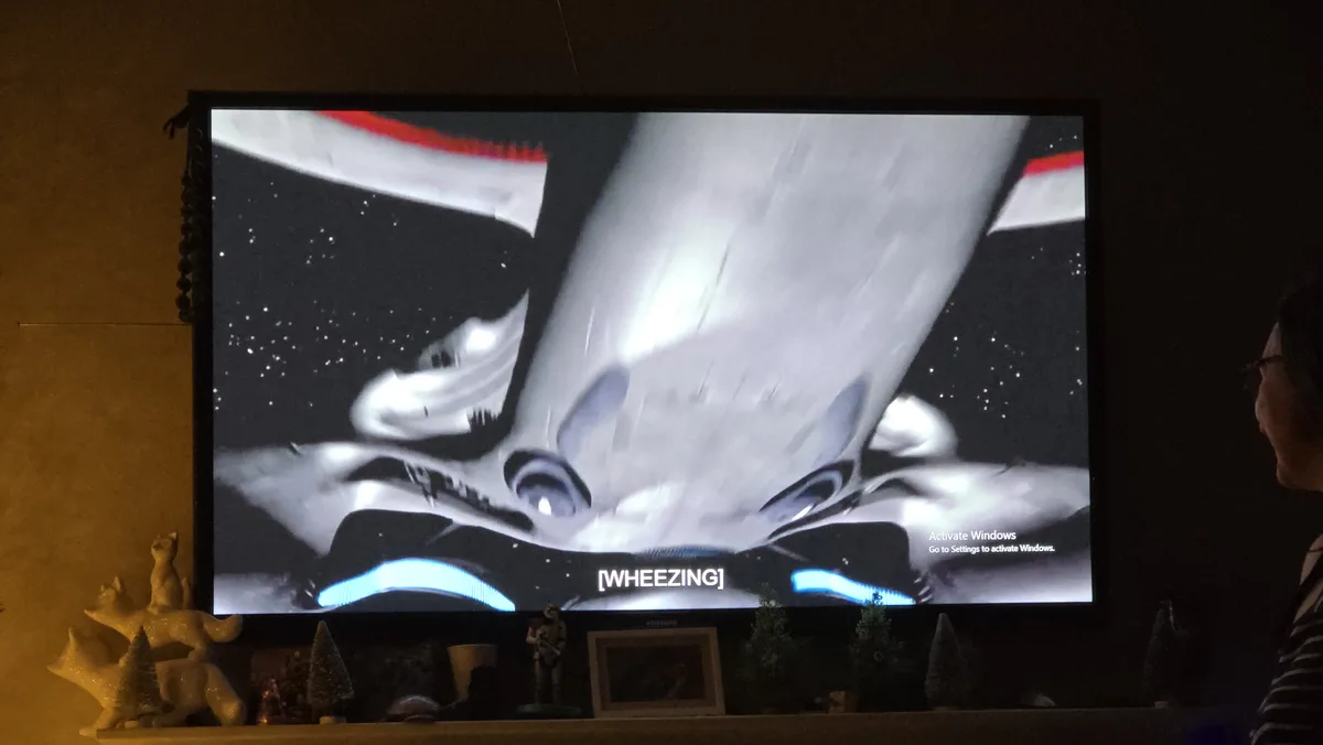 A person watches a TV screen displaying a sci-fi movie scene with a spaceship and stars, overlaid with the text '[WHEEZING]'…