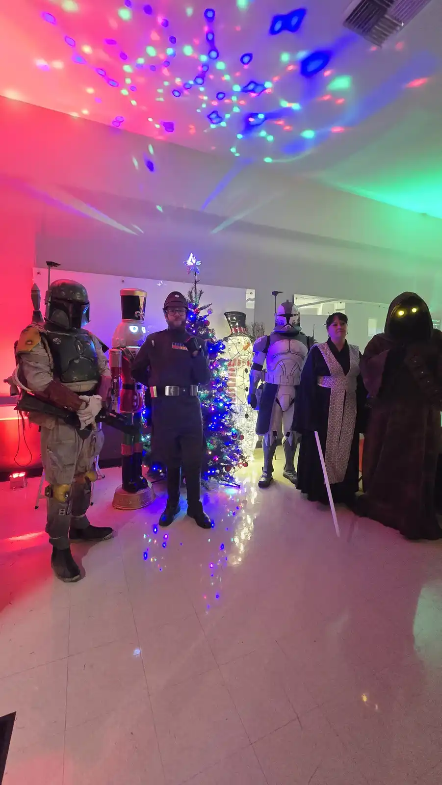 A group of people dressed as Star Wars characters, including Boba Fett, a Clone Trooper, a Jedi, and a Sith Lord, stand in a…
