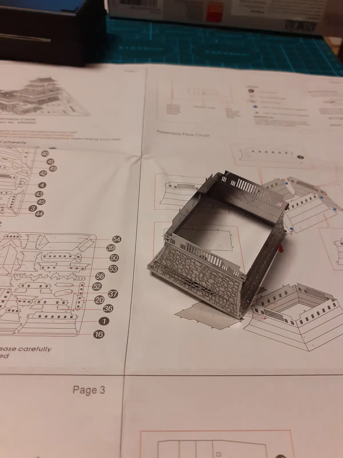 A partially assembled metal 3D puzzle castle sits on its instruction manual, which shows diagrams and part numbers. The text…