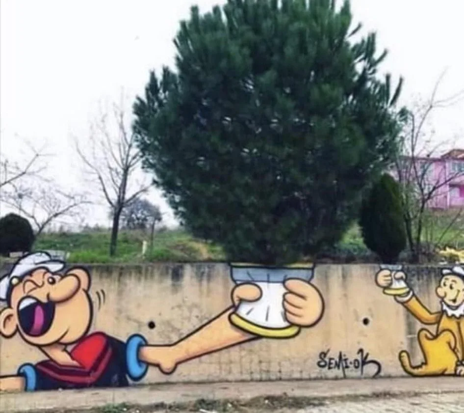 A real pine tree grows out of a painted cartoon character's hand holding a pot, as if it were a potted plant, while another…