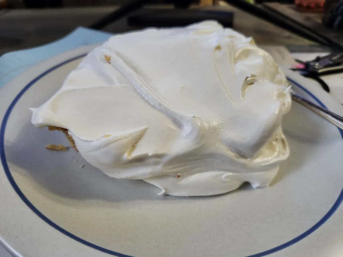 A close-up photo shows a slice of pie with an excessive, lumpy layer of white meringue covering most of it, sitting on a…