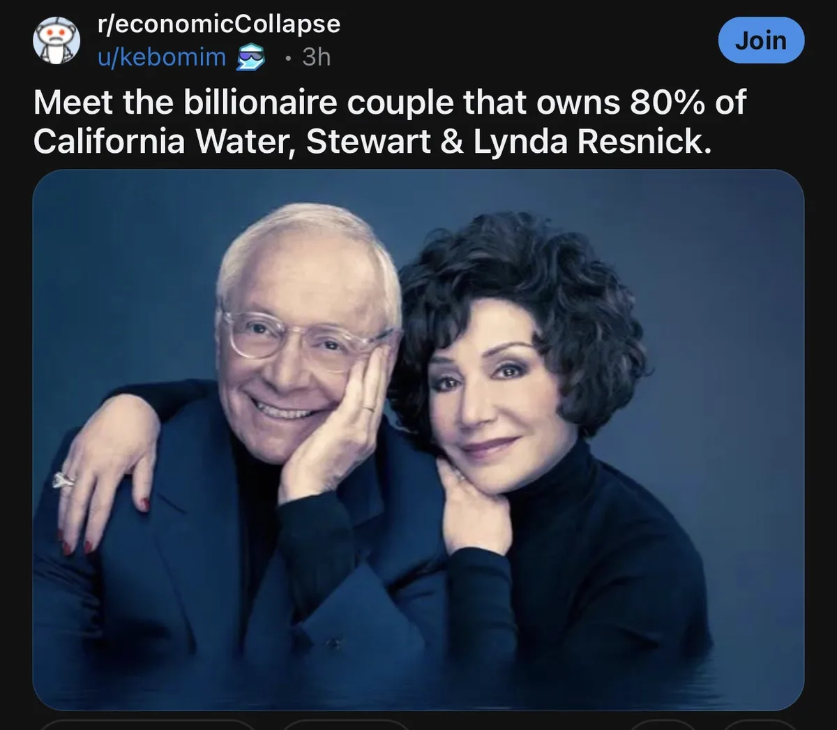 A professionally taken portrait shows an older man and woman posing closely together against a dark blue background. The…