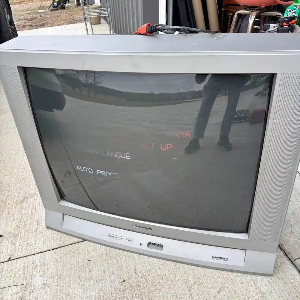 An old silver Panasonic CRT television sits outdoors on a concrete surface, its screen displaying red and blue setup text…