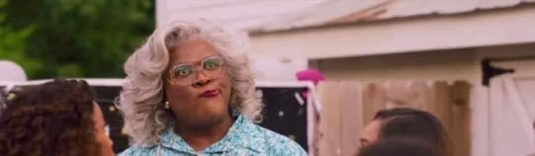 A woman with curly gray hair and glasses makes a skeptical, slightly disgusted facial expression while looking upward. She…