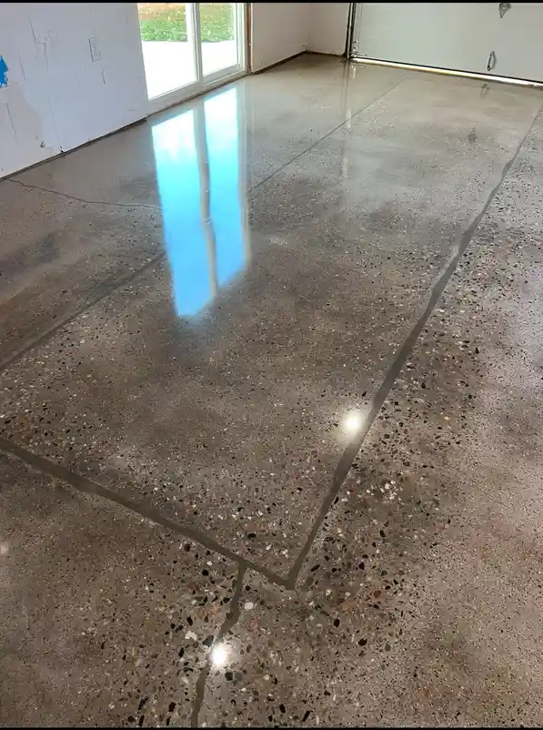 A photo of a polished, speckled concrete garage floor with visible seams and a bright blue reflection from a window…