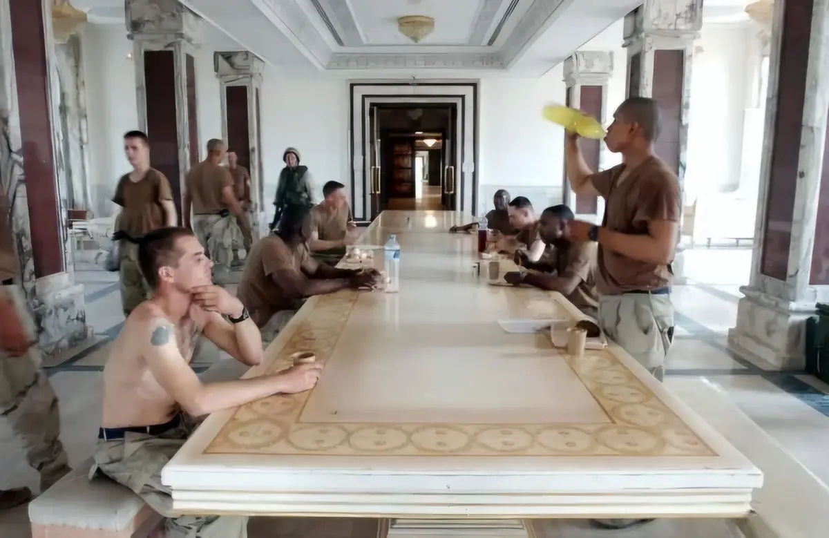 A group of soldiers in a grand, ornate dining hall sit around a long marble table. One soldier in the foreground, shirtless…