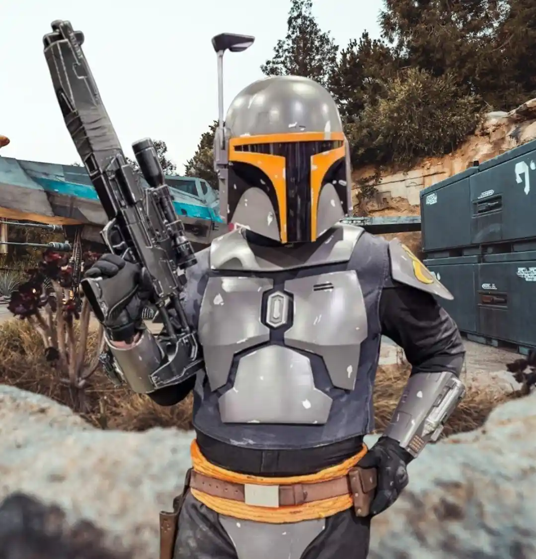 A person in a detailed Boba Fett costume, complete with helmet, armor, and blaster, stands outdoors in a Star Wars-themed…