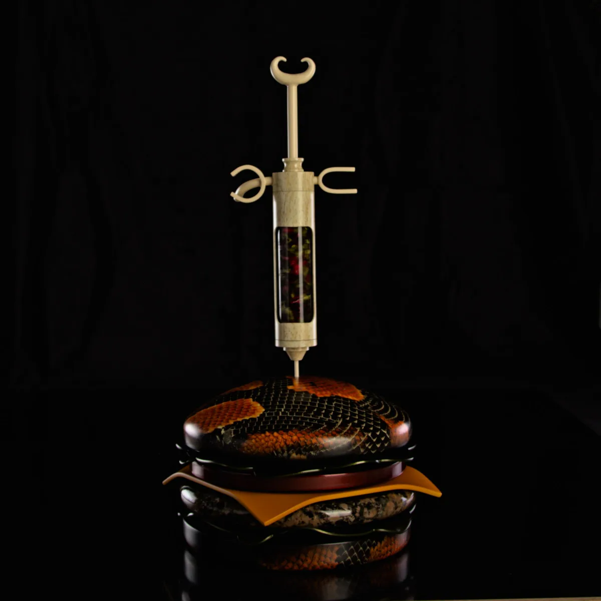 a highly stylized, luxury burger with snake-skin textured buns, a cheese slice, and a wooden syringe filled with rose petals…