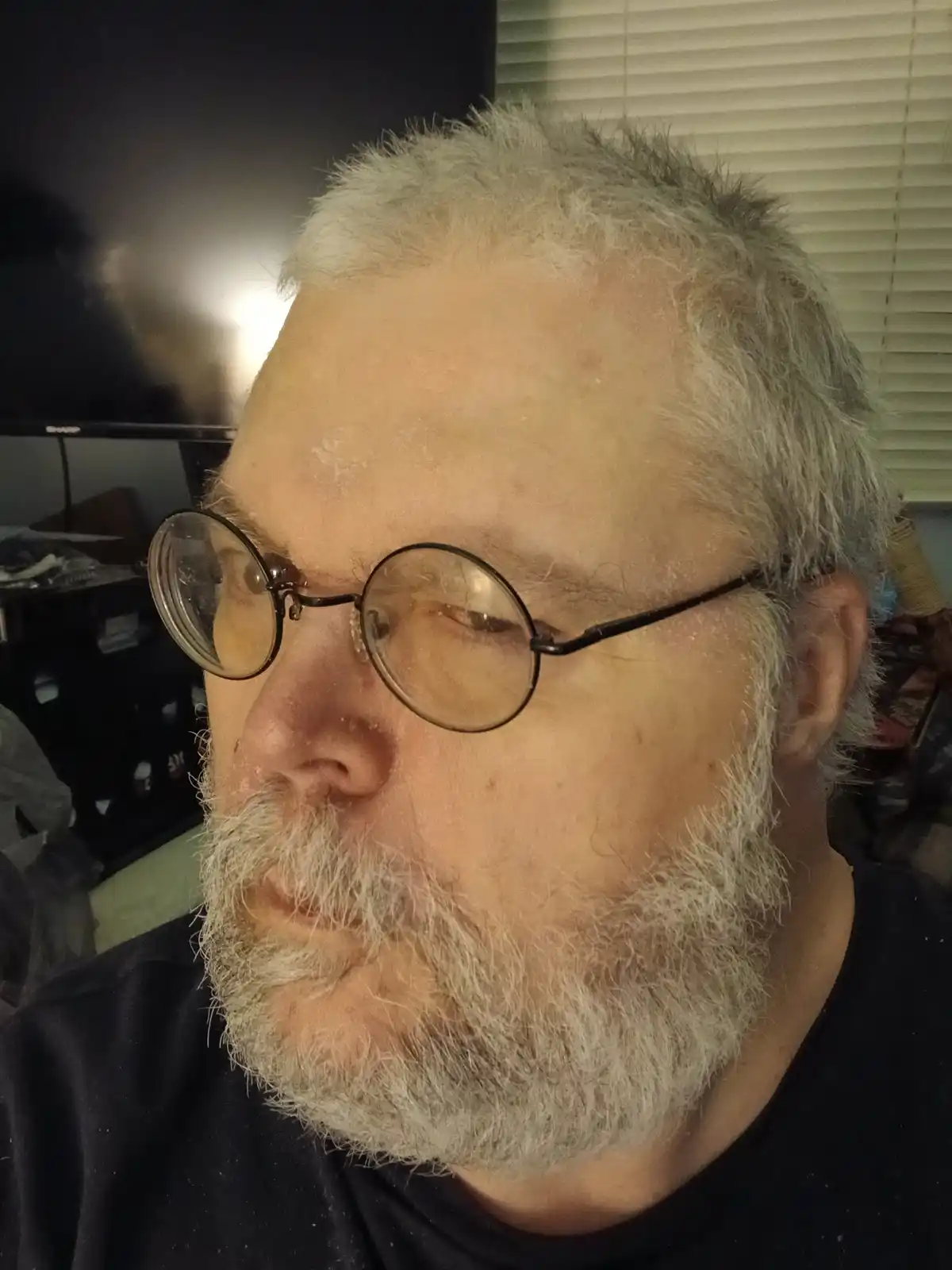 A close-up photo of a middle-aged man with gray hair and beard, wearing round glasses, looking slightly to the side. His…