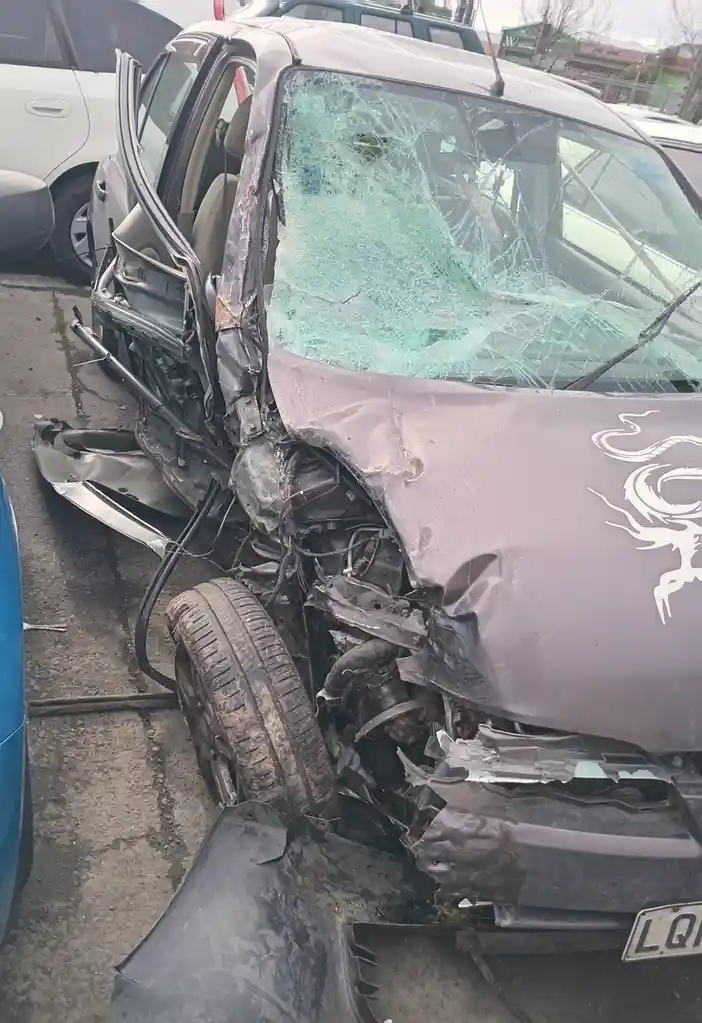 A heavily damaged purple car with a shattered windshield, crumpled front end, and exposed engine components sits in a…