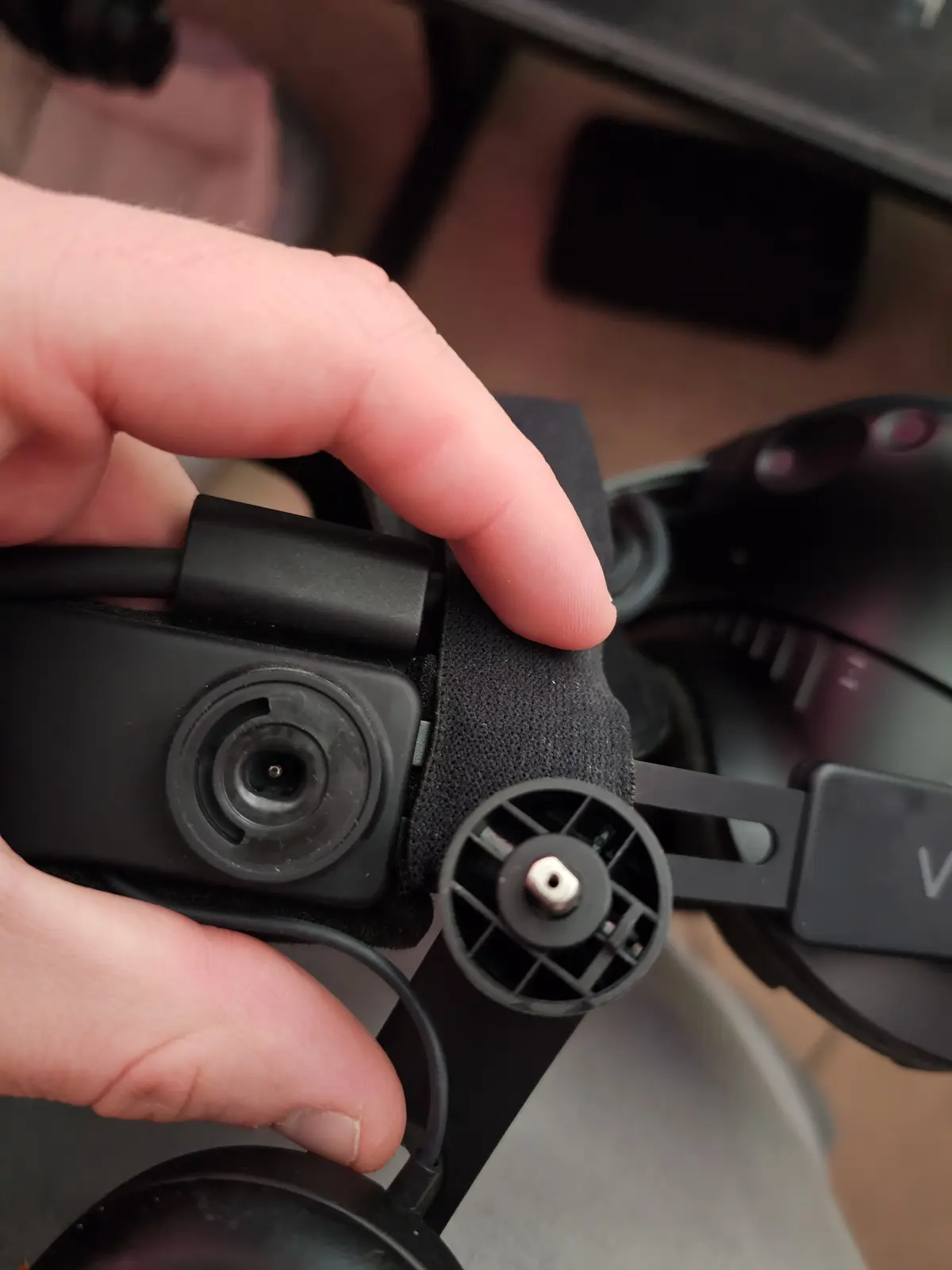 A close-up photo shows a person's hand holding a black headset with a detached microphone component. The mic has a circular…