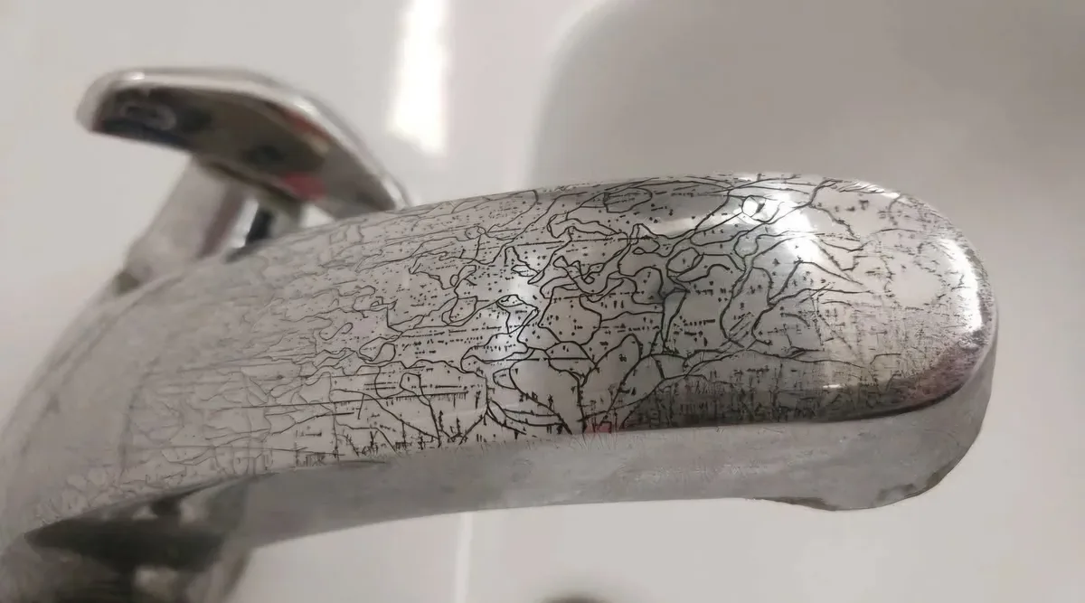 a close-up photo of a chrome faucet handle with a detailed, hand-drawn map of the world etched into its surface, showing…