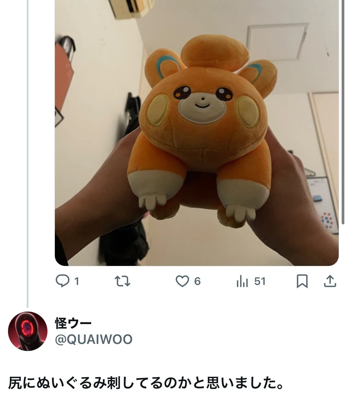 A person holds up an orange, round, plush toy resembling a Pokémon character with large ears and a smiling face. The…