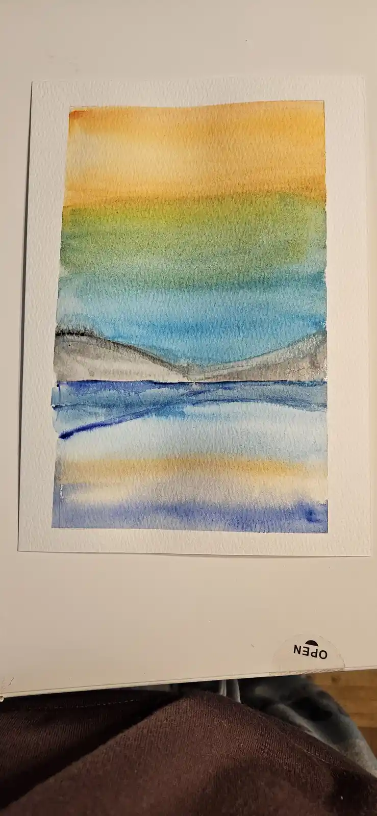 A watercolor painting on textured paper depicts a layered landscape with horizontal bands of color: orange-yellow sky, green…
