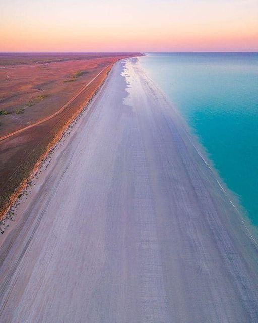 An aerial view shows a long, narrow strip of light-colored sand separating a turquoise ocean on the right from a…