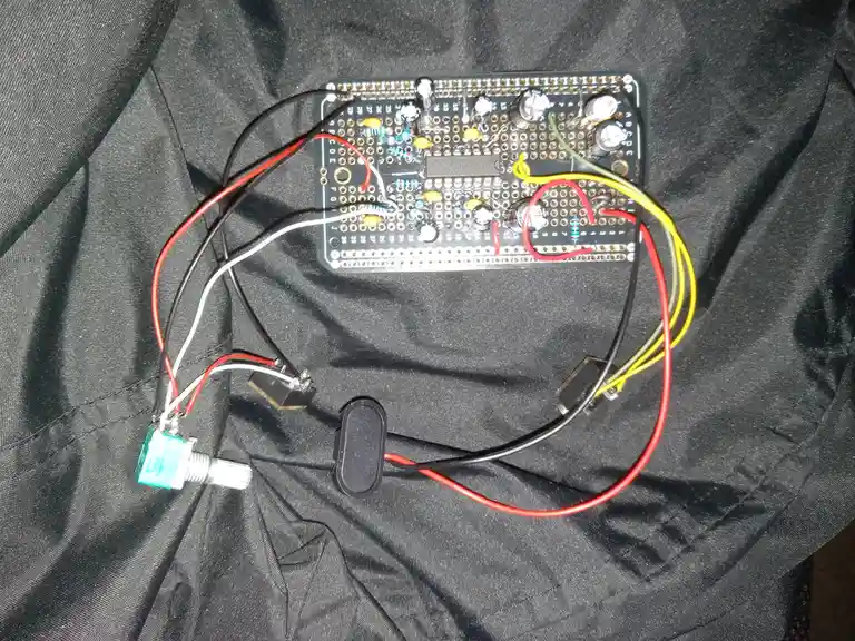 A homemade electronic circuit on a breadboard with various components and colorful wires, resting on a black fabric surface…