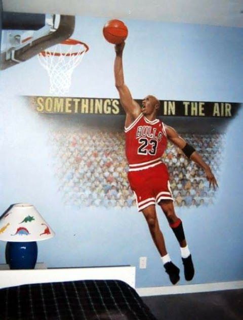 A bedroom wall mural depicts Michael Jordan in his iconic red Chicago Bulls #23 jersey, mid-air dunking a basketball toward…