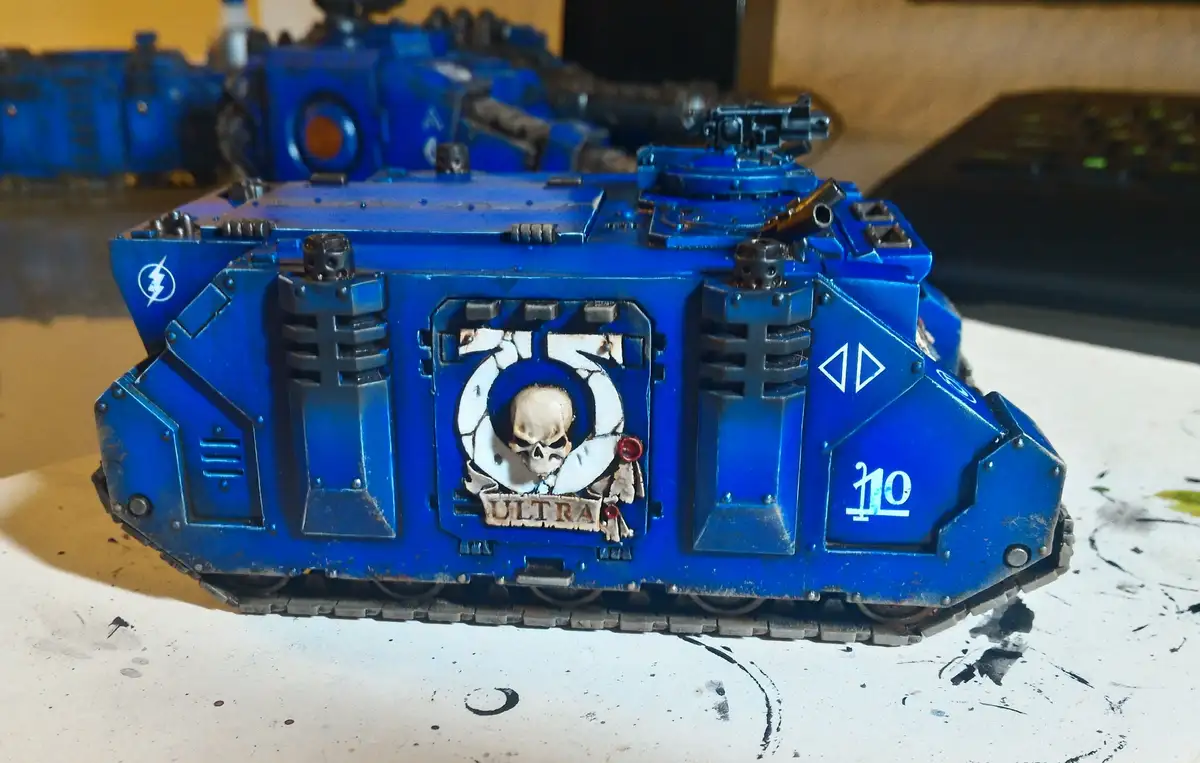 A close-up of a blue-painted, heavily detailed miniature tank model with a skull emblem and the word 'ULTRA' below it…