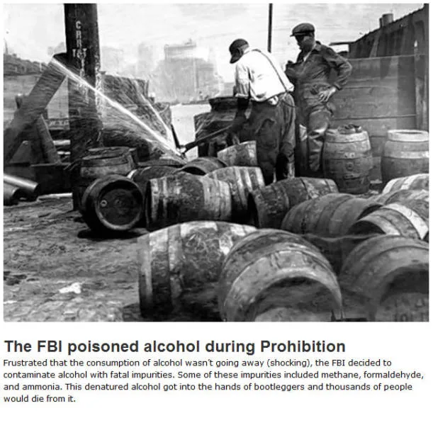A black-and-white historical photo shows two men in work clothes spraying a liquid from a hose into a pile of wooden…