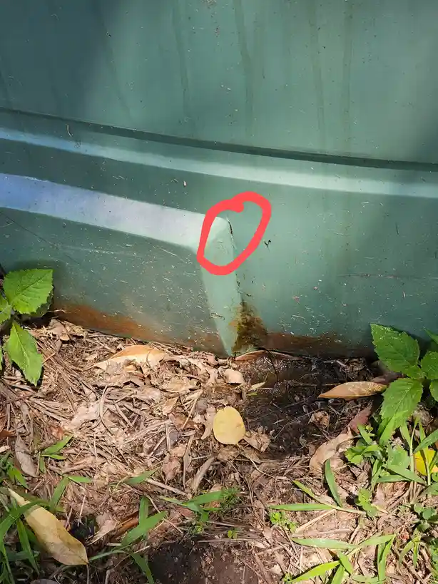 A close-up photo shows the bottom corner of a green metal shed, where a small, rust-stained area is circled in red. The…