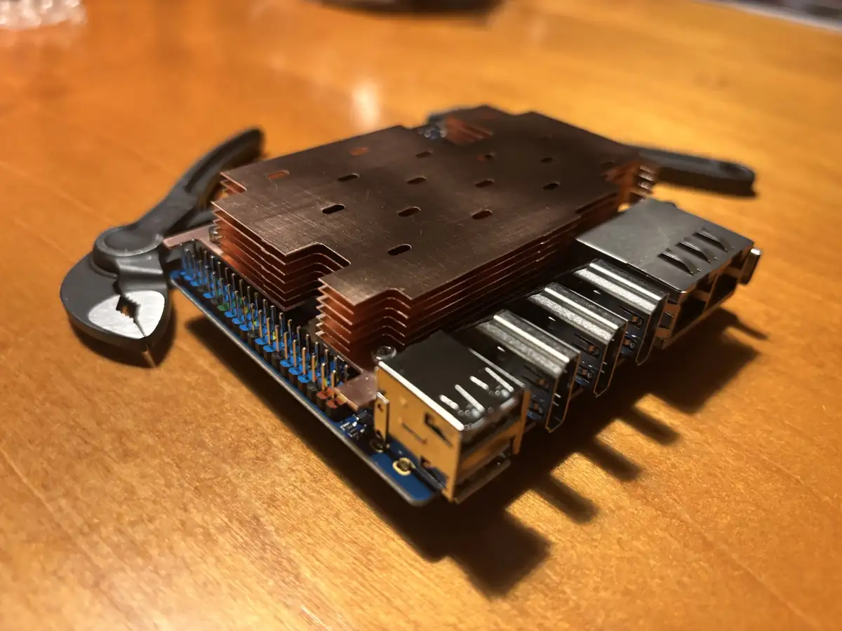 A close-up photo shows a small blue circuit board, likely a Raspberry Pi, with an absurdly oversized copper heatsink stacked…