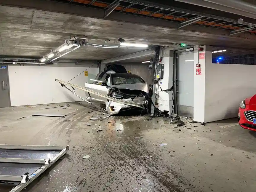A silver car is severely damaged in an underground parking garage, having crashed into a pillar and ripped off part of the…