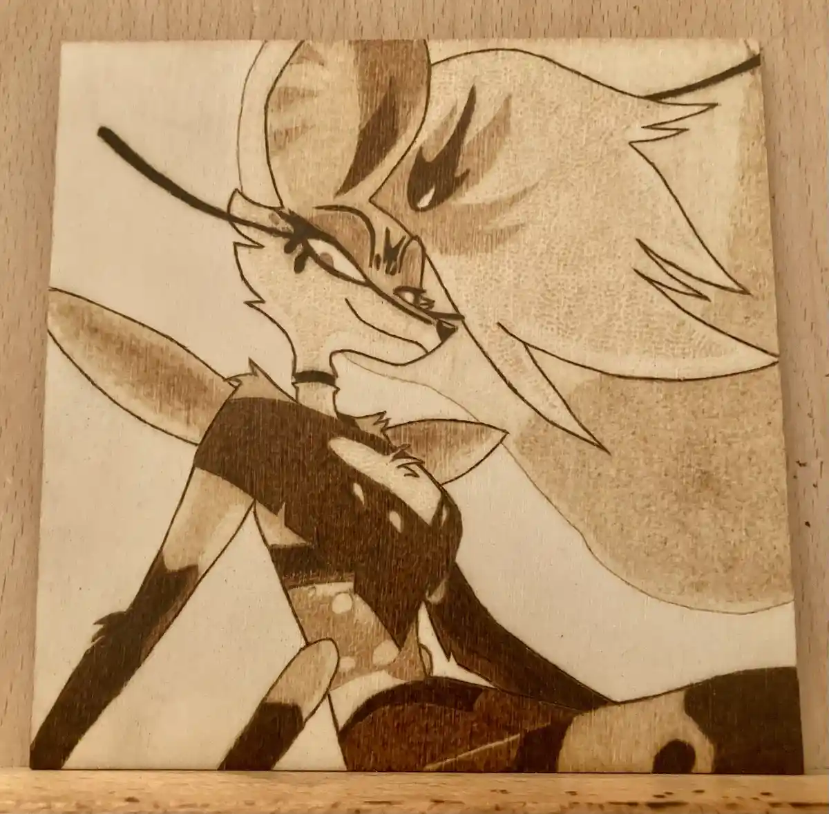 A wood-burned artwork depicts a stylized anthropomorphic fox character with long hair, wearing a dark top and holding a…